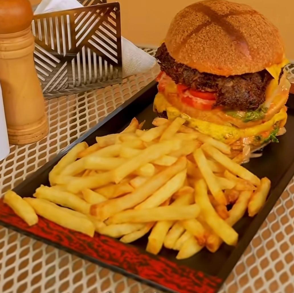 Stacked beef burger with melted cheese, lettuce, tomato, and house sauce with fries